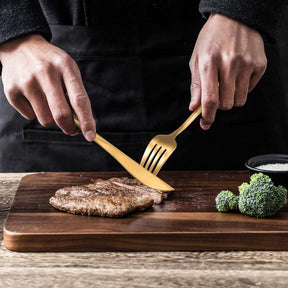 Talheres de ouro de aço inox cortando um bife de boi em cima de uma tábua de cortar carne.